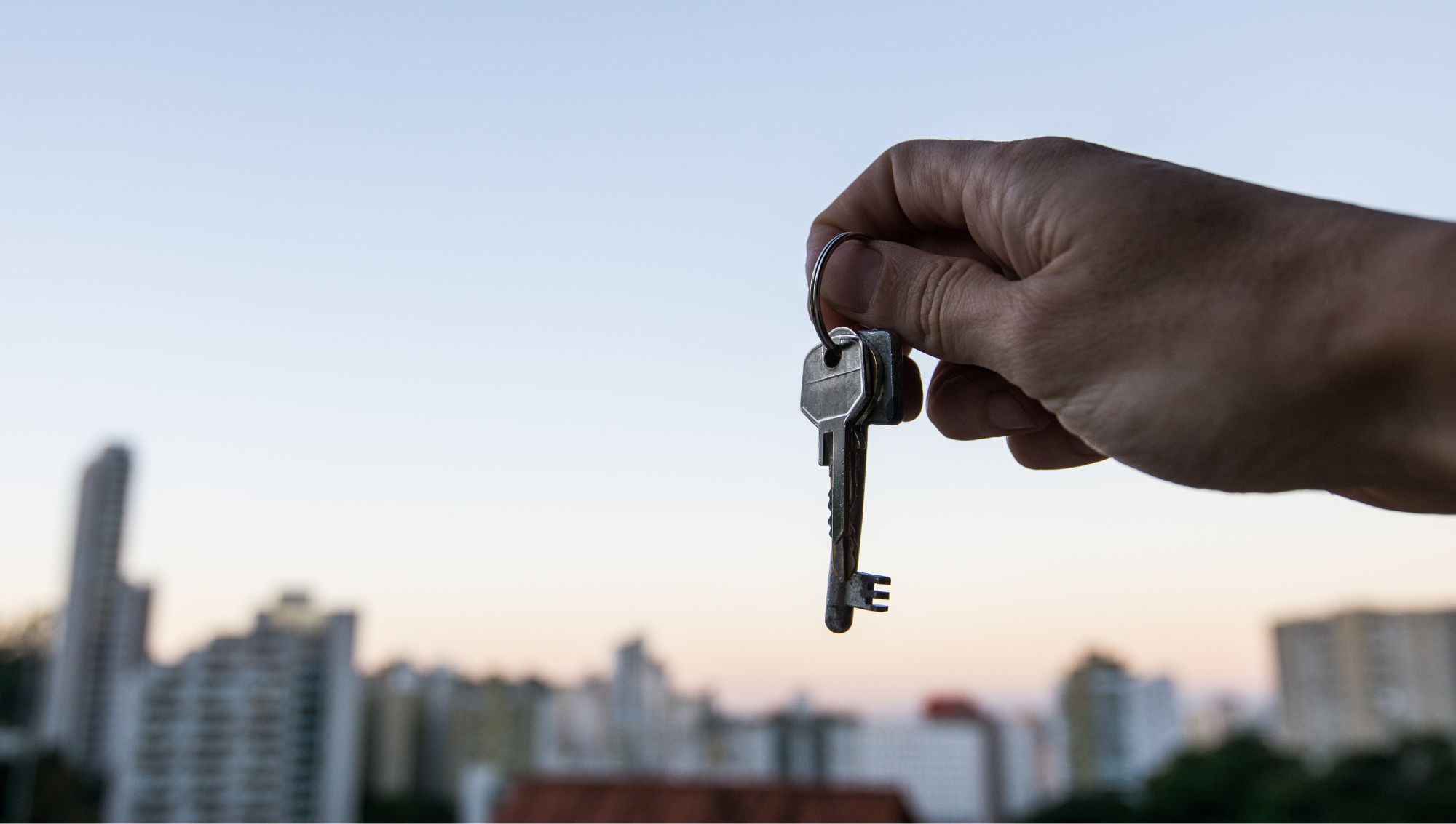 Person holding house keys with a cityscape background, symbolizing a new home purchase or successful mortgage closing at Strategy Home Loans.